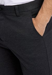 Donkere grijze broek van geweven stof, met een platte voorkant, zijzak en een gladde textuur. De tailleband is voorzien van riemlussen.