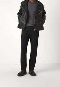 Schwarze Leder-Bikerjacke mit silbernem Zubehör, grauer strukturierten Pullover und schwarze Hose. Abgerundet mit schwarzen Stiefeletten.