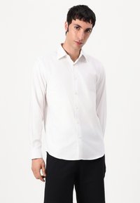 White long-sleeve shirt made of lightweight fabric, featuring a classic collar, button front, and straight hem. Suitable for casual wear.