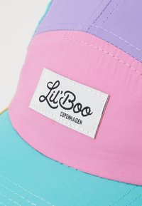 Spalvota kepurė, kurios dalys pagamintos iš levandų, rožinės ir teal spalvų audinio. Pridedama firminė balta etiketė su užrašu "Lil' Boo Copenhagen" juodu tekstu.