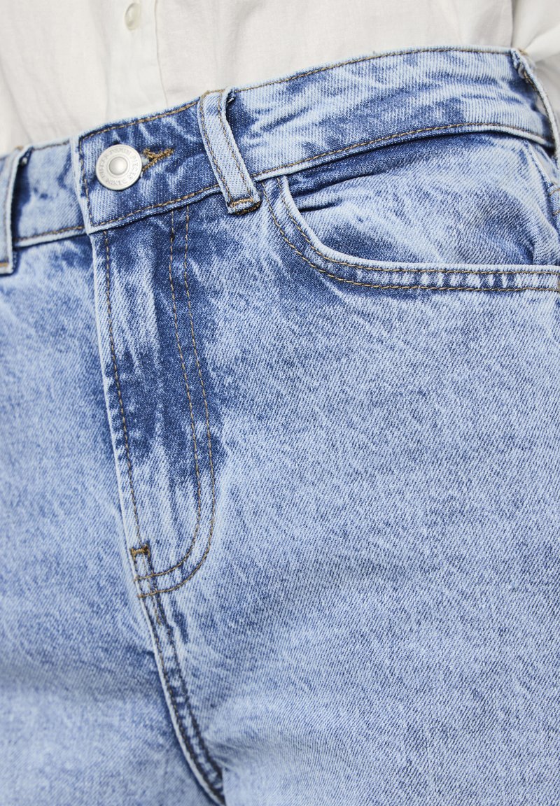 Lichtblauwe spijkerbroek met een vervaagde was, voorzien van een voorkleur, riemlussen en een zilveren knoopsluiting. De textuur is glad met zichtbare stiksels.