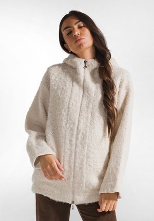Crème-kleurige zip-up jas van een textuur fleece materiaal, met een capuchon en brede mouwen. Kenmerkt zich door een vooraanlopende rits en een relaxte pasvorm.