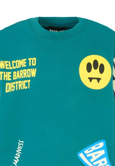 Miętowa bawełniana koszulka z żółtym napisem "WITAJ W DZIELNICY BARROW", okrągłą żółtą grafiką i różnymi dekoracyjnymi naszywkami.