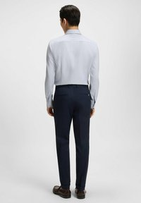 Ljust blå långärmad skjorta med ett subtilt mönster, kombinerad med mörkblå byxor och avslutad med bruna skor. Bakifrån visas outfitens passform.