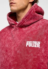 Bordeaux hoodie met een gestructureerde afwerking, voorzien van een witte opdruk met de slogan "ESCAPE FROM THE POLIZIE" aan de linkerkant. Met capuchon ontwerp.