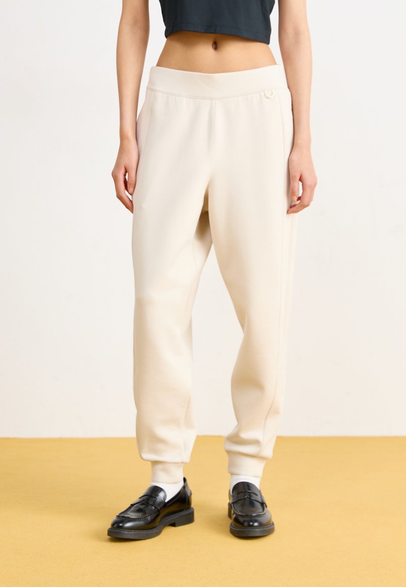 Svetlo bež, udobni hlače za prosti čas s elastičnim pasom in stranskimi žepi. Narejene so iz gladkega, mehkega blaga in imajo preprost dizajn.