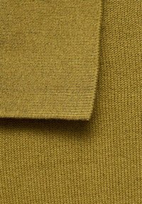 Olivgrön stickad tyg med en texturerad yta. Materialet har en jämn, fin väv och en mjuk finish. En vikt kant är synlig.