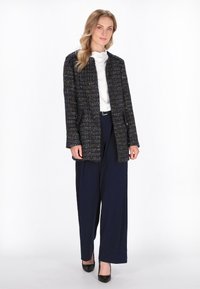 Giacca testa di moro con texture e pizzichi multicolori, apertura frontale, maniche lunghe, abbinata a pantaloni navy a gamba larga e tacchi neri.
