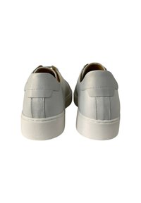 Sneakers bianchi in pelle con una texture liscia, forma arrotondata e suole in gomma bianca a contrasto. Presentano cuciture sottili e linguette posteriori.