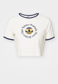 Bílý zkrácený tričko s námořnickým lemem a krátkými rukávy, se zaobleným modro-žlutým logem Adidas na přední straně.