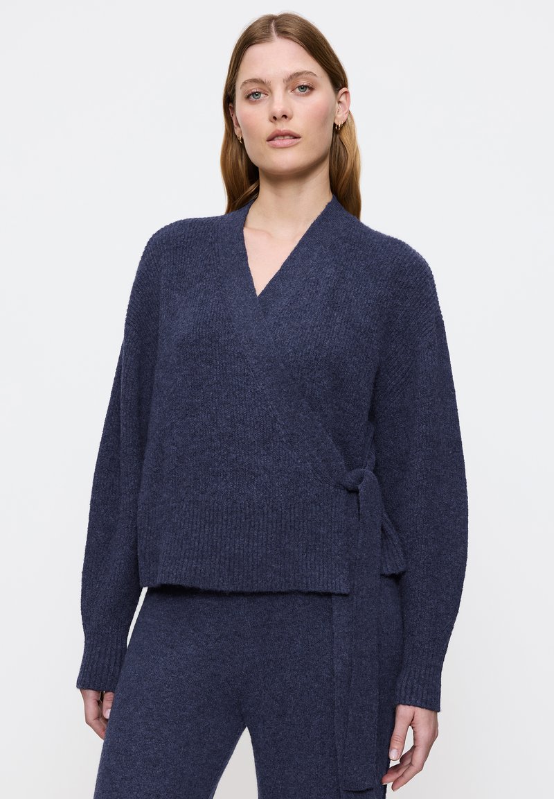 Cardigan avvolgente navy realizzato in un materiale a maglia texture, caratterizzato da maniche lunghe, scollo a V profondo e vita annodata. Fit complessivo rilassato.