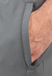 Grå atletiske shorts med en sidelomme med en skjult lynlås, lavet af glat, letvægtsstof. Synlig syningsdetalje på lommen.