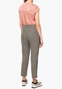 Blouse rose en satin à manches courtes associée à un pantalon à carreaux noir et blanc ; les deux vêtements ont une coupe ajustée et des détails de texture subtils.