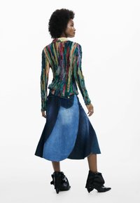 Pull tricot coloré et texturé à manches longues ; associé à une jupe en denim multi-tons avec des panneaux incurvés et des bottines noires.