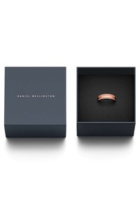 Ruusu-kultainen sormus makaa tummansinisessä laatikossa, jossa on mattapintainen viimeistely. Laatikon kannessa on kultainen, kohokuvioitu brändinimi ja musta samettinen sisustus.