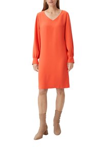 Orangenes knielanges Kleid mit V-Ausschnitt und langen, puffärmeligen Ärmeln. Glatter Stoff mit lockerer Passform. Tragen mit hellbeigen, hohen Stiefeletten.