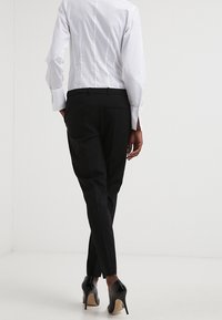 Pantalones negros ajustados combinados con una camisa blanca entallada, con un tejido suave, piernas estrechas y zapatos de tacón alto.