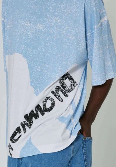T-shirt a maniche corte con un design testurizzato blu e bianco, caratterizzato da un audace testo grafico nero lungo il lato. Taglio casual e ampio.