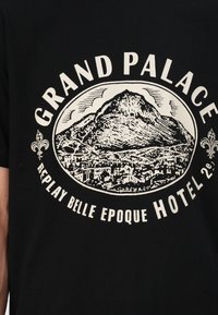 Schwarzes Baumwoll-T-Shirt mit weißem Grafikdruck eines Berges und einer Stadtsilhouette sowie dem Text "GRAND PALACE REPLAY BELLE EPOQUE HOTEL."