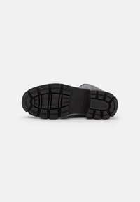 Semelle de chaussure en caoutchouc noir avec des crampons profonds pour l'adhérence ; surface texturée présentant un motif de rainures et de crêtes pour une meilleure prise.
