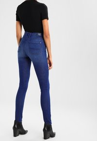 Smala jeans i mörkblå denim med hög midja, bakfickor och en mjuk textur, parat med en svart åtsittande skjorta och ankelstövlar.