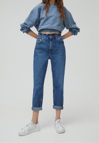 Blå kort sweatshirt med vida ärmar, matchad med hög midja, avslappnade blå denimjeans med upprullade fållar och vita sneakers.