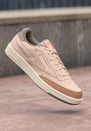 Lichtroze suède sneaker met een beige suède hiel, crème rubberen buitenzool en perzikaccenten. Kenmerkt een geperforeerde neus en een merkgetailleerde tong.