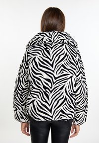 Doudoune imprimé zèbre avec capuche, featuring un tissu noir et blanc, un grand col et des poignets élastiques pour un ajustement serré.