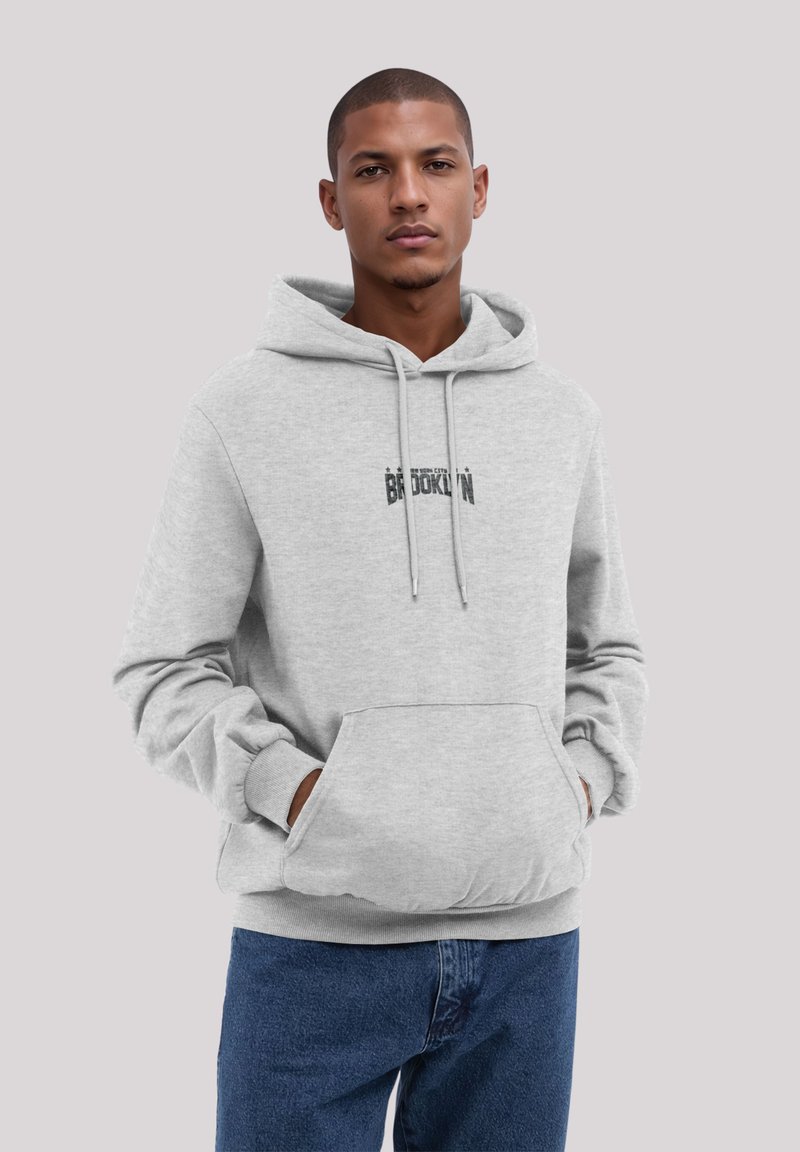 Gray hoodie with a front pocket, drawstrings, and a printed "Brooklyn" logo. Paired with blue jeans, featuring a simple, casual fit.