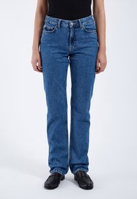 Jeans de mezclilla azul claro con un diseño de pierna recta, cinco bolsillos y detalles de costura sutil. Cierre frontal con botón. Tejido texturizado.