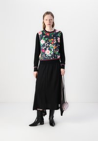 Long black skirt paired with a floral-patterned sweater featuring pink accents. Model wears black pointy boots and holds a small purple bag.