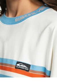 Kortärmad, krämfärgad t-shirt i bomull med blå, orange och bruna ränder. Inkluderar en blå ribbad krage och en svart logotypplåst.