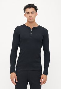 Crna dugosleeve henley majica napravljena od rebrastog materijala, s okruglim izrezom, tri dugmeta na prednjem dijelu i uskim manžetama.