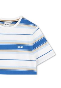 Pruhované tričko v bílé, modré a béžové barvě. Má krátké rukávy a kulatý výstřih. Bílé logo "BOSS" na levé části hrudi. Bavlněný materiál.