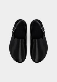 Μαύρα δερμάτινα παπούτσια χωρίς κορδόνια με στρογγυλεμένο σχέδιο, που διαθέτουν ρυθμιζόμενο λουράκι με αγκράφα και λεία υφή επιφάνειας.