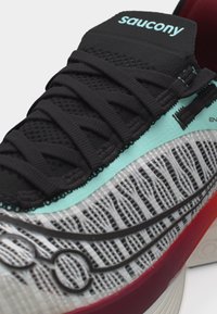 Κοντινό πλάνο μαύρου παπουτσιού τρεξίματος Saucony με επάνω μέρος από δίχτυ, λεπτομέρειες σε μέντα πράσινο και κόκκινο στη μεσαία σόλα.