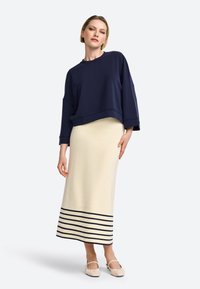 Felpa over-size blu marino con maniche ampie abbinata a una gonna crema con righe orizzontali blu marino all'orlo. Scarpe beige senza laccio.