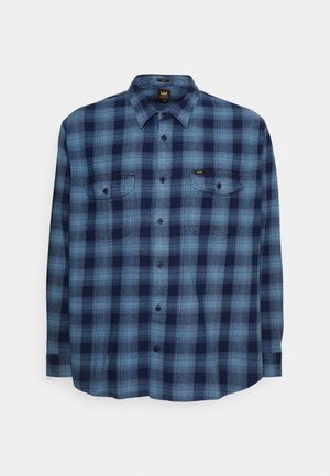Camisa de manga larga con botones, a cuadros en azul y azul marino, con dos bolsillos en el pecho y cuello, extendida sobre un fondo blanco.