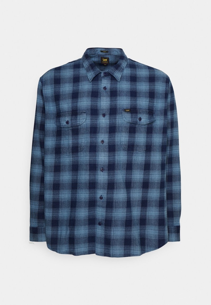 Chemise à manches longues à carreaux bleus et bleu marine avec deux poches poitrine et un col, posée à plat sur un fond blanc.