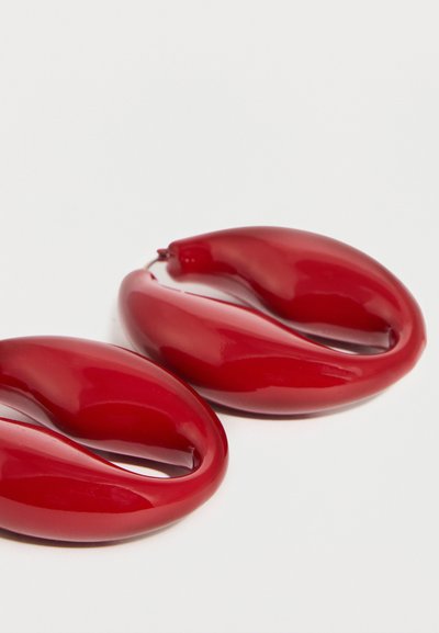 Κόκκινα γυαλιστερά σκουλαρίκια σε σχήμα οβάλ κρίκου με ομαλή, καμπυλωτή σχεδίαση σε λευκό φόντο.