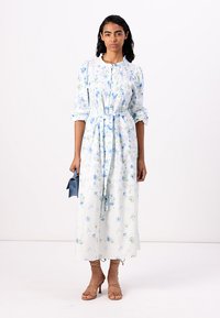 Vestido floral de mangas longas em branco com padrões azuis e verdes, com cintura ajustada, frente de botões e silhueta midi reta.