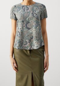 Top de manga corta en verde con un patrón de paisley en azul marino, beige y rosa. Escote redondo, tejido suave y corte relajado.