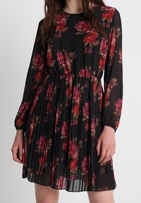 Abito a stampa floreale nero con fiori rosa e rossi. Maniche lunghe, gonna plissettata, vita elasticizzata, tessuto leggero. Collo rotondo.