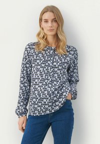 Camicia con bottoni caratterizzata da un motivo geometrico nei toni di blu, navy e bianco; maniche lunghe con polsini arricciati; orlo curvato; realizzata in tessuto leggero.