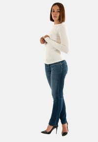 Top bianco a maniche lunghe abbinato a jeans skinny blu. Tacchi alti neri. Tessuto liscio, design aderente e dettagli di cucitura sottili.