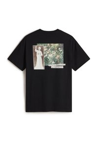 Sort bomulds T-shirt med et collageprint på ryggen: en figur der holder en stav og en livlig blomsterscene med tekst nedenfor.