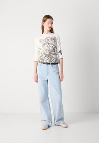 Witte blouse met lange mouwen en panterprint, gecombineerd met lichtblauwe wijde spijkerbroek. De outfit bevat een zwarte riem en zilveren schoenen. Glad textuur.