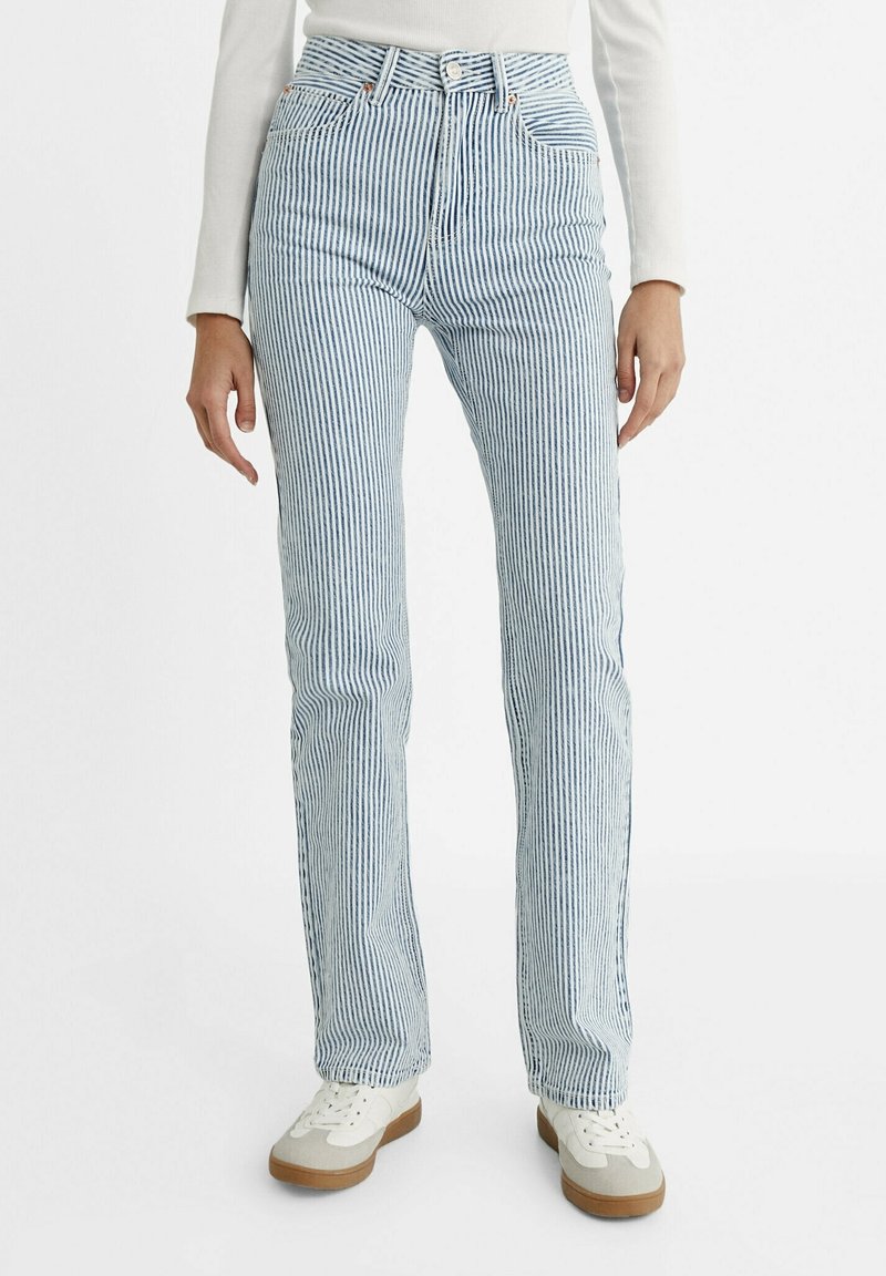 Jean en denim rayé bleu et blanc avec une taille haute, une jambe droite et une fermeture classique à boutons. Porté avec des baskets blanches.