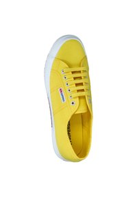Sneaker in tela gialla con suola in gomma bianca, sei asole per i lacci, tomaia testurizzata e un piccolo logo rosso e blu di lato.