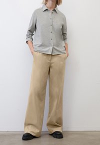 Camicia grigia button-up con colletto, maniche lunghe e vestibilità rilassata, abbinata a pantaloni beige larghi e scarpe chunky nere.